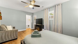 Ein Schlafzimmer mit Bett, Sofa, Fernseher, Deckenventilator und Vorhängen.