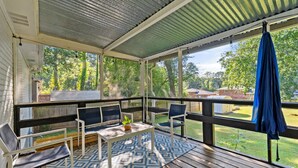 Eine überdachte Terrasse im Freien mit einem gemusterten Teppich, Sitzgelegenheiten und Blick auf den Garten.