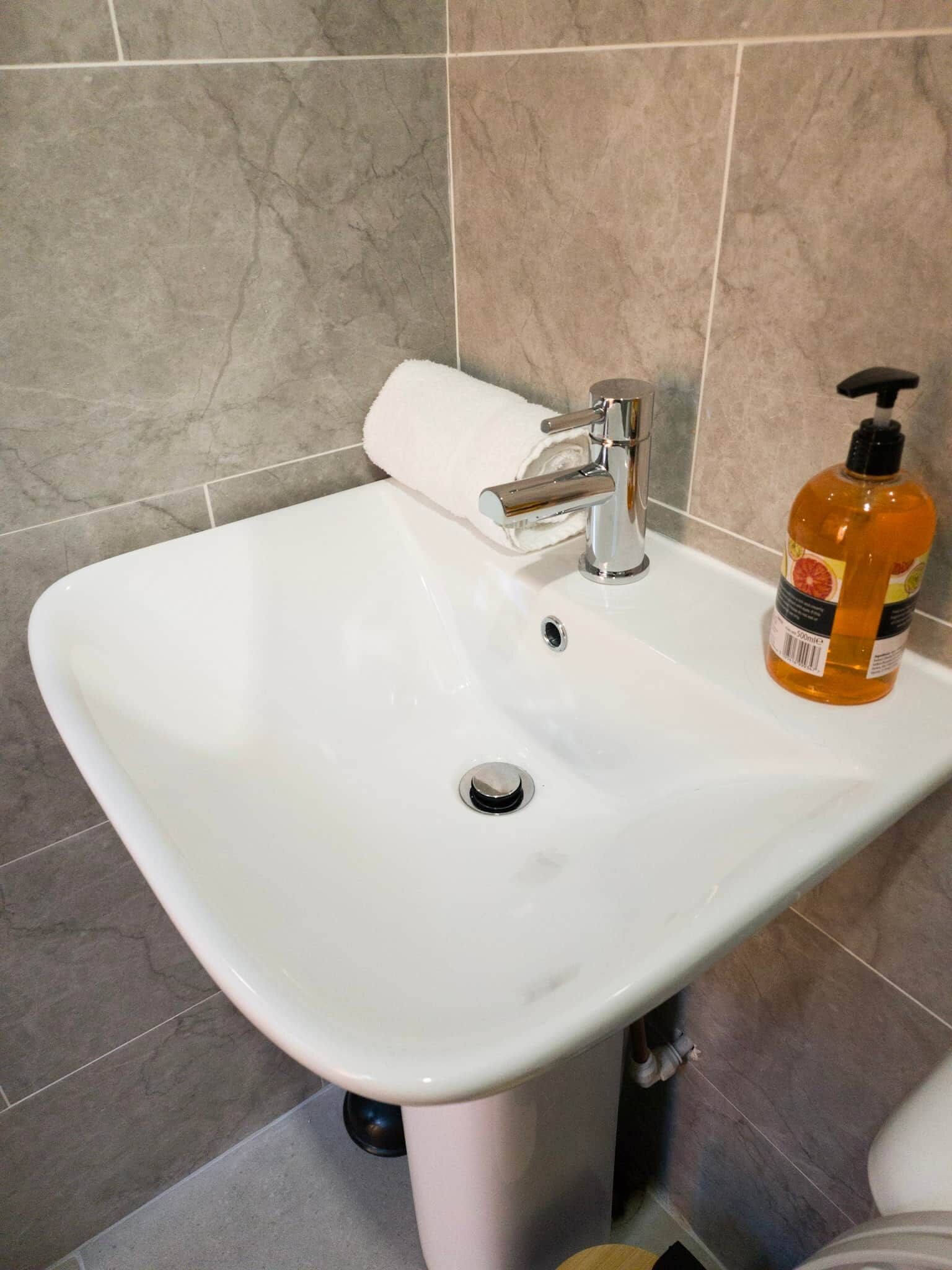 A bathroom sink with a white basin, chrome faucet, and a bottle of orange liquid soap.