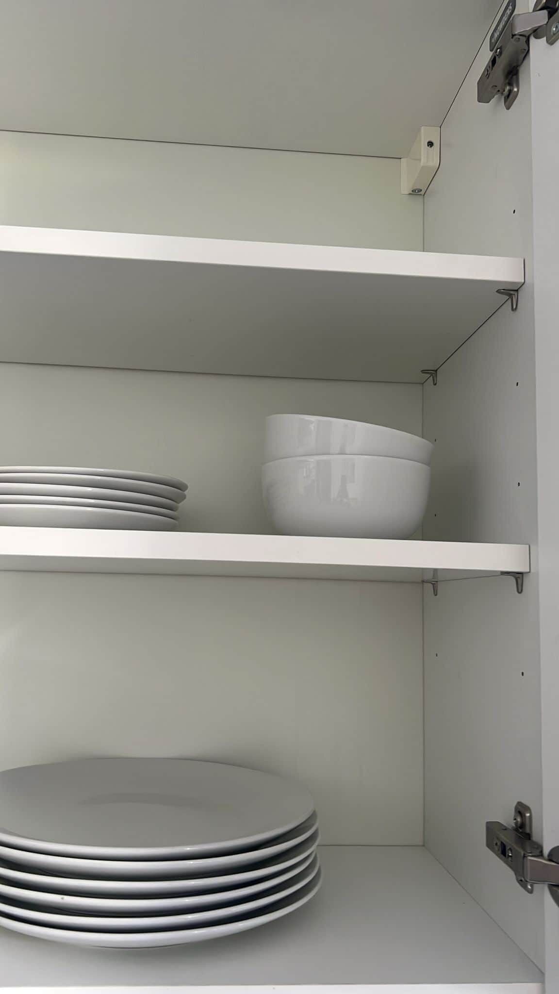 Une cuisine avec des étagères blanches, un saladier blanc et des assiettes empilées.