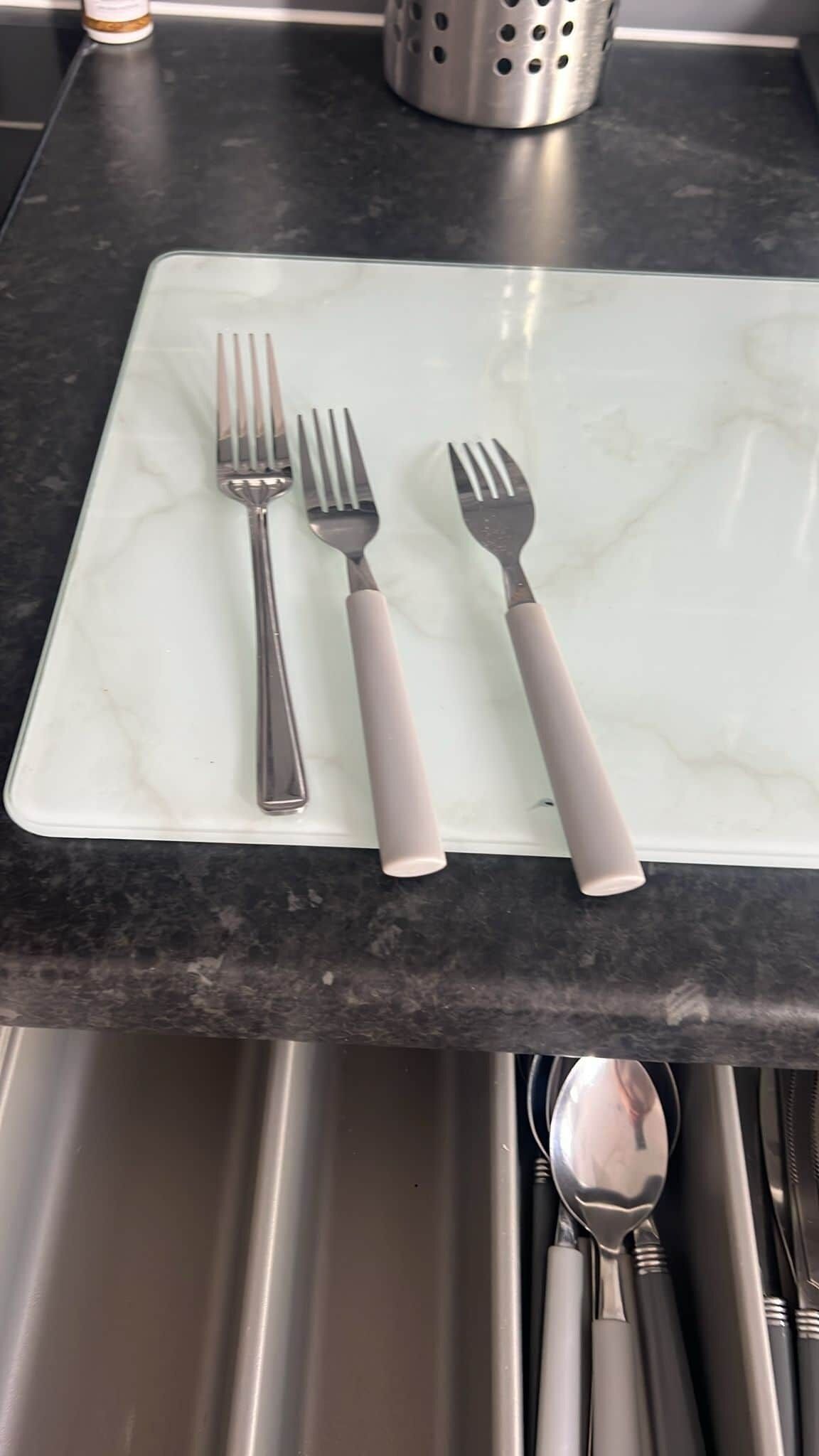 A white marble serving tray with two forks and a knife on a dark countertop.