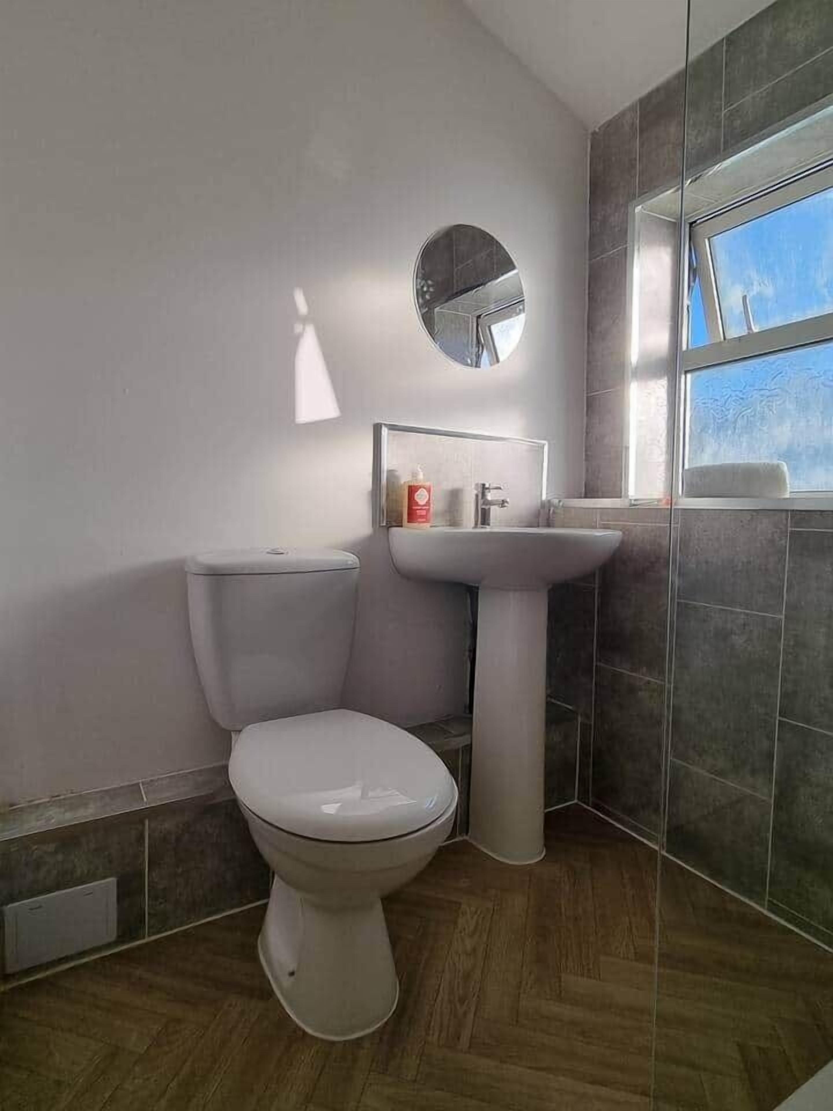 Une salle de bain équipée de toilettes, d’un lavabo, d’un miroir et d’une fenêtre.