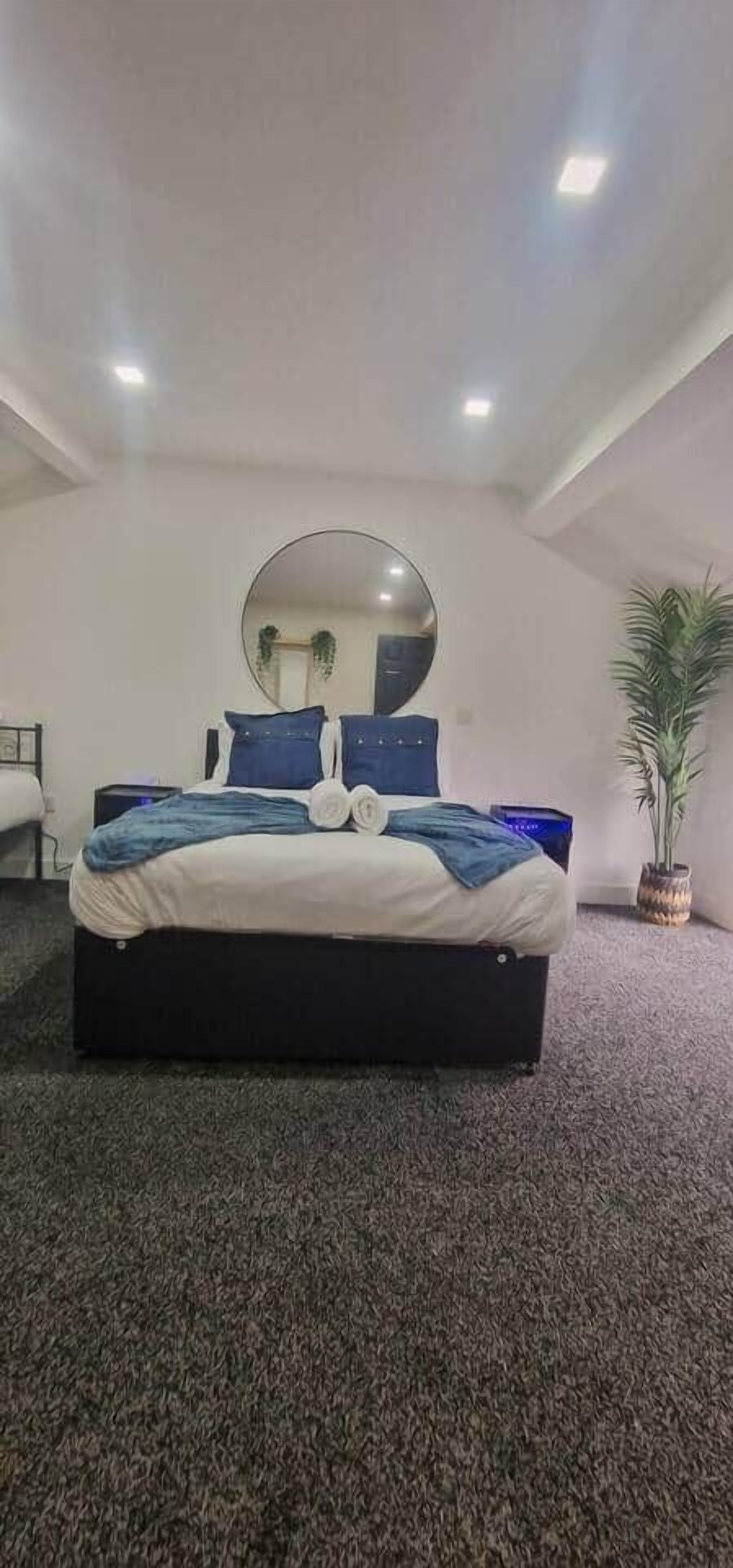 A modern bedroom with a large bed, a round mirror, and a potted plant.