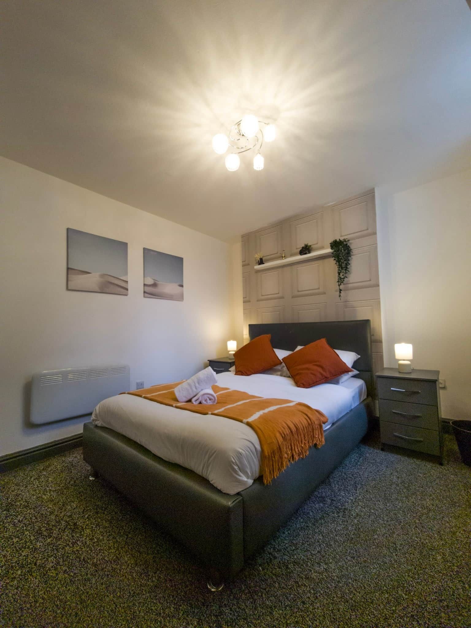 Une chambre bien rangée, avec un lit, des tables de chevet, un radiateur et des étagères fixées au mur.
