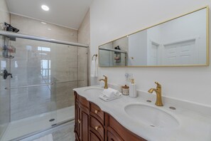 A modern bathroom with a glass shower enclosure, dual sinks with gold fixtures, and a large mirror. - Stunning ocean-view cottage minutes from Olympic (Port Angeles)