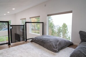 A modern bedroom with a large window, a sliding glass door, and a view of trees. - Stunning ocean-view cottage minutes from Olympic (Port Angeles)