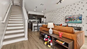 En moderne stue med trappe, et køkken i baggrunden, et fjernsyn og en væg med et Mickey Mouse-mønster.