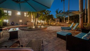 Une cour avec des fauteuils de jardin, des parasols et une piscine.