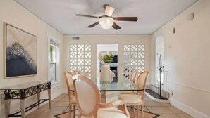 Un coin repas comprenant une table en verre, quatre chaises, un ventilateur de plafond et un panneau décoratif mural.