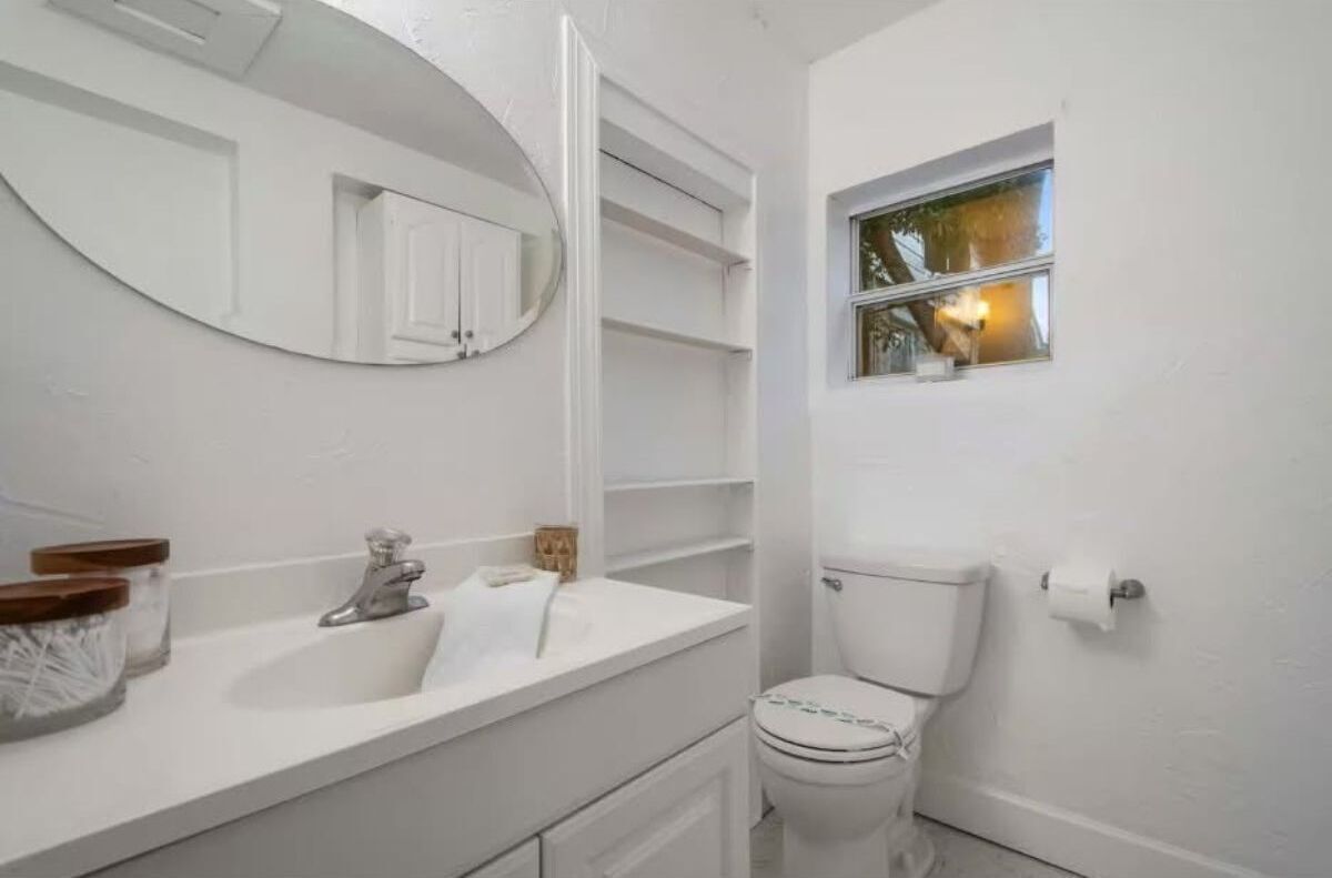 A bathroom with a white sink, a mirror, a toilet, and a window.