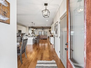 A modern kitchen with wooden flooring, a dining area with chairs, a central island, and a view into the living room. - The Bourbon Embassy at Twin Creeks (Winchester)