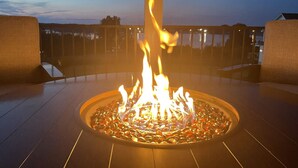 Een ronde vuurplaats met een centrale paal, omgeven door een metalen rand, op een houten terras.