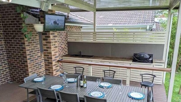 Eine Außenpatio mit Ziegelwand, einem an der Wand montierten Fernseher, einem Grill und einem Tisch für vier Personen mit Stühlen.