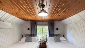 Ett rum med två sängar, trägolv, en takfläkt och ett fönster med gardiner.