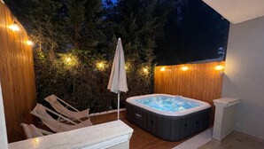 Ein Whirlpool mit Holzwand und einer Holzterrasse mit Liegestühlen.