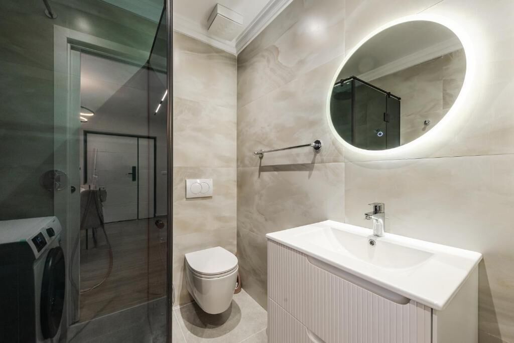 A modern bathroom with a glass shower enclosure, a toilet, a sink with a mirror, and a towel rack.