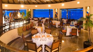 Um restaurante com mesas redondas, cadeiras e vista para o oceano.