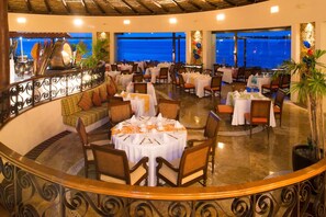 Un restaurante con mesas redondas, sillas y vistas al océano.