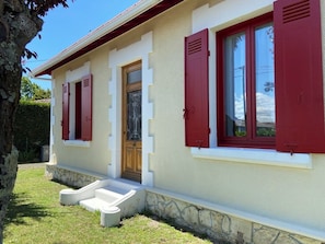 Ein Haus mit Steinunterbau, einer Haustür und roten Fensterläden.