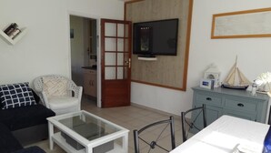 A living room with a sofa, a coffee table, a TV, a cabinet, and a door leading to another room. - Gite la Pinassotte - GUJAN-MESTRAS (GUJAN-MESTRAS)