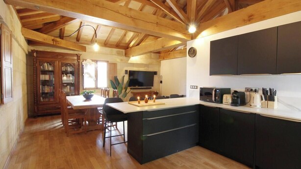 Cucina con travi in legno, zona pranzo con tavolo e sedie, e isola nera con elettrodomestici.