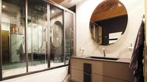 Un bagno moderno con doccia vetrata, uno specchio rotondo e un piano d'appoggio in marmo.