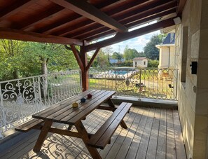 A covered outdoor area with a picnic table and a view of a swimming pool and a small building in the background. - La Ruche - CAMBES - Gîte (CAMBES)