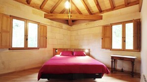 Camera da letto con soffitto in legno, pareti in pietra, un letto con biancheria rossa e mobili in legno.