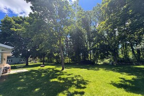 A backyard with a lawn, a barbecue grill, a picnic table, and a stone wall. - Racers Homebase: Mins to Road America, Golf & Dining (Howards Grove)