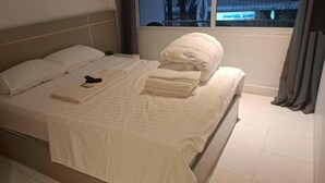 Una cama bien hecha con almohadas y toallas dobladas, un control remoto y una ventana con cortinas.