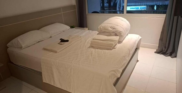 Una cama bien hecha con almohadas y toallas dobladas, un control remoto y una ventana con cortinas.