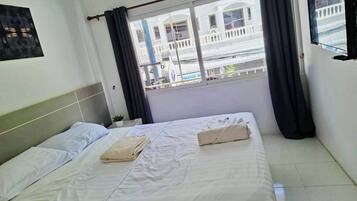 A hotel room with a bed, curtains, a window, and a view of a building outside.