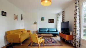 A living room with a sofa, armchair, coffee table, TV, and patterned curtains. - Gîte du Pitchouret - BELIN BELIET (BELIN BELIET)