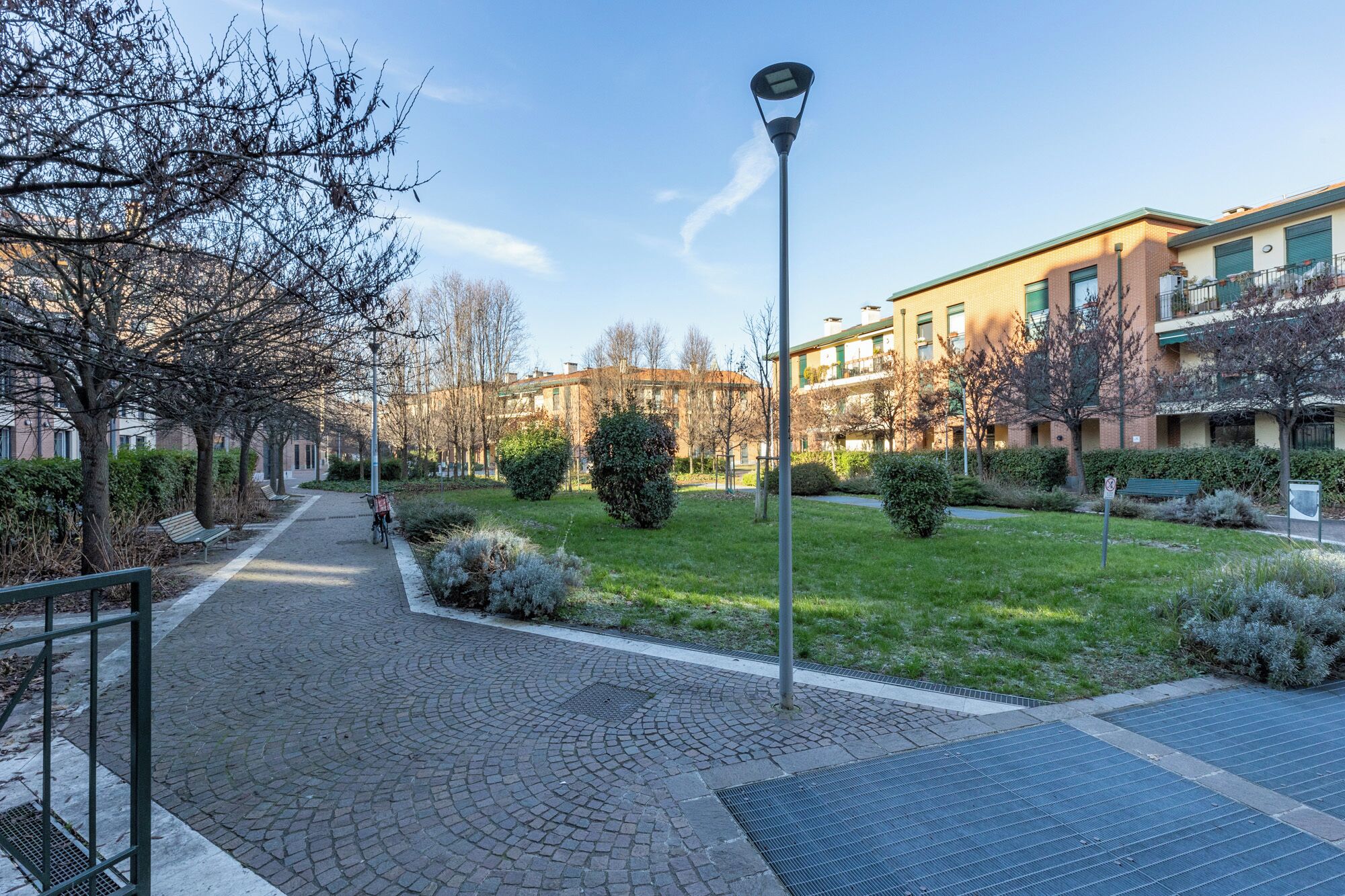 Ein gepflasterter Weg mit einem Fahrrad, einer Straßenlaterne und einem Gebäude mit mehreren Fenstern und Balkonen.