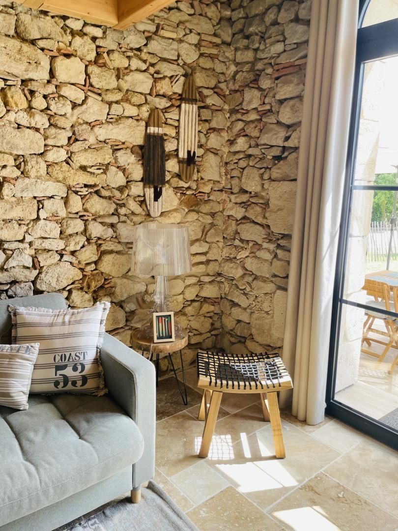 Ein Zimmer mit einer Steinsäule, einem grauen Sofa mit gestreiften Kissen, einem kleinen Holzschemel und einer Lampe auf einem Beistelltisch.