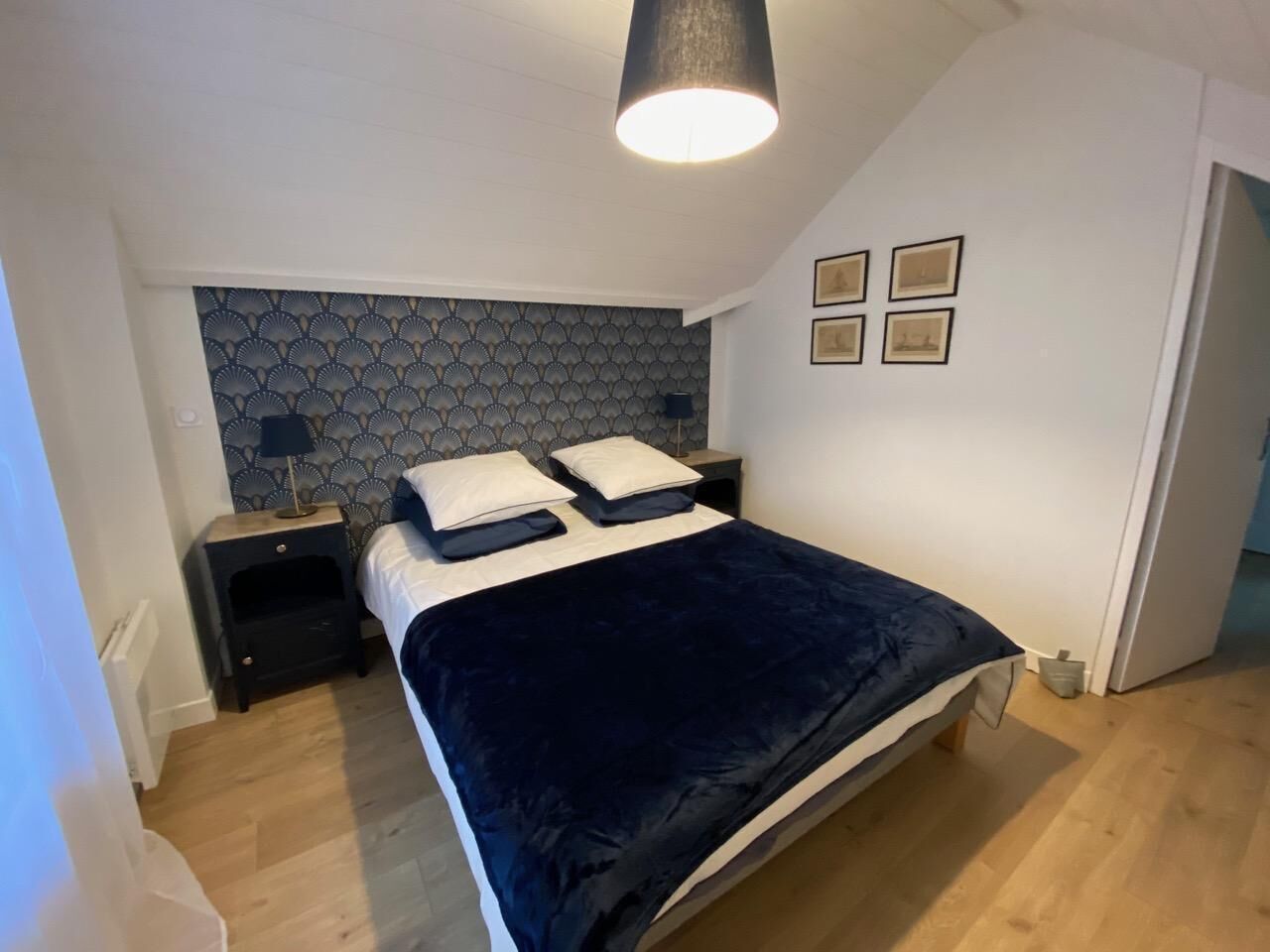 Een slaapkamer met een bed, nachtkastjes, een hoofdbord met een patroon en een plafondlamp.