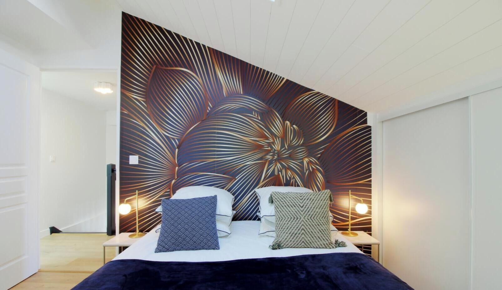 A bedroom with a large wall mural, a bed with two pillows, bedside tables with lamps, and a wooden floor.