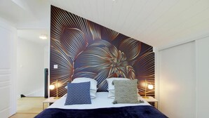 Une chambre avec un grand décor mural, un lit avec deux oreillers, des tables de chevet avec des lampes et un plancher en bois.