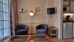 Quarto com duas cadeiras, luminária de chão, televisão, micro-ondas, cafeteira e máquina de lavar.