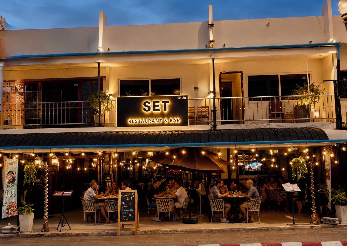 A restaurant with outdoor seating, a sign reading 'SET RESTAURANT & BAR,' and a menu board.