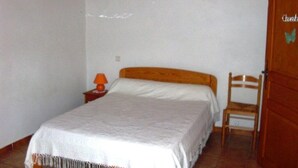 Een slaapkamer met een bed, een stoel, een nachtkastje, een lamp en een deur.