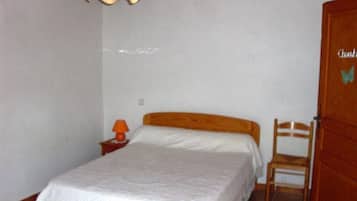 Un dormitori amb llit, cadira, tauleta de nit, làmpada i porta.