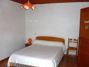 A bedroom with a bed, a chair, a nightstand, a lamp, and a door. - La Terrasse Neuve in La Teissonnière (SAINT HILAIRE DE LAVIT)