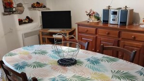 Een eethoek met een ronde tafel, stoelen, een televisie en een houten kast.