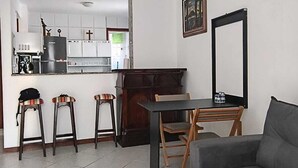 Un espacio habitable compacto con kitchenette, una zona de comedor con mesa y sillas, y un sofá gris.