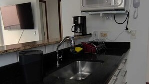 Una cocina con encimera negra, pileta de acero inoxidable, cafetera y microondas.