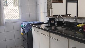 Una cocina con armarios blancos, encimera negra, un fregadero y una ventana con vistas a edificios.