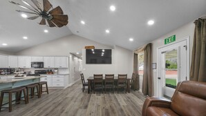 Eine geräumige Küche mit weißen Schränken, ein Essbereich mit Tisch und Stühlen, ein braunes Ledersofa und ein Deckenventilator.