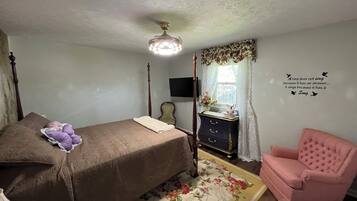 A bedroom with a four-poster bed, a dresser, a pink armchair, a floral rug, and a wall quote.