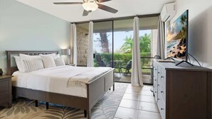 A bedroom with a bed, a ceiling fan, a TV, a dresser, and a balcony with a view. - 2 bedroom updated Kihei condo, AC, walk to beach, shops, & dining (Kihei)
